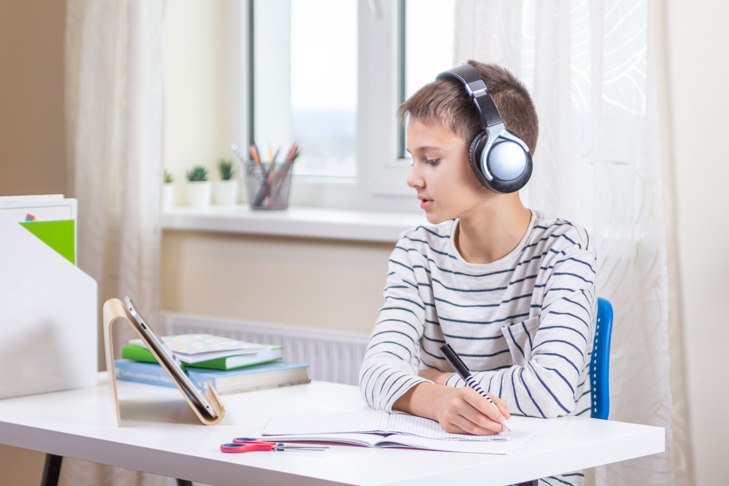 Image used on readable handwriting course page of boy writing whilst wearing to headphones