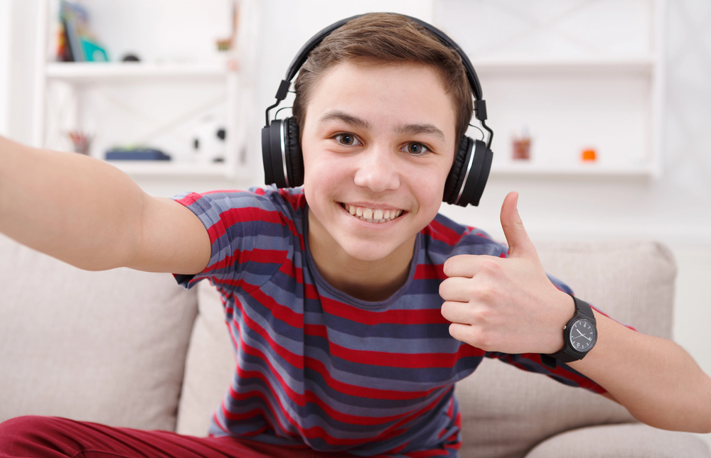 An image of a smiling teenage boy sitting on a sofa with headphones on and thumbs up, used for handwriting practice club to show enjoyment of doing the club.